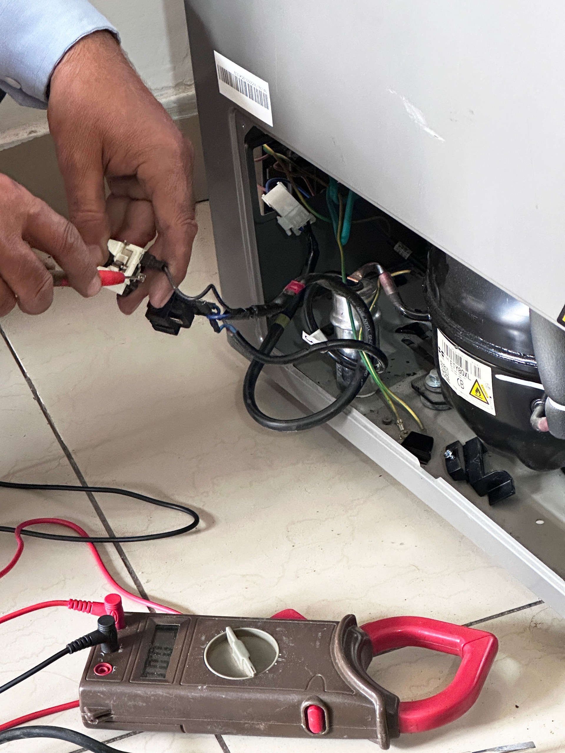 Close-up image of unrecognisable handyman checking electric current of freezer in kitchen, recharging gas compressor, gas canister, refrigerant